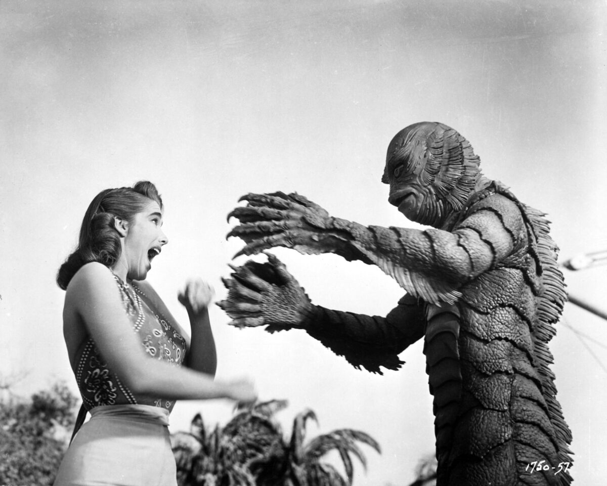 a woman in a swimsuit freaking out while a rubbery fish man reaches out like he's going to muss up her hair