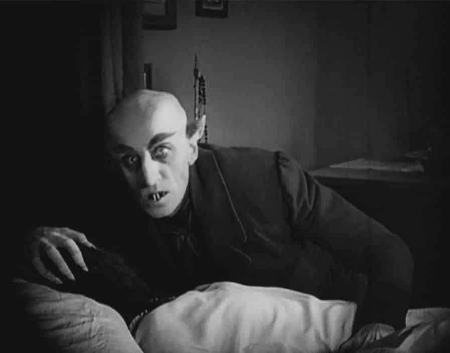 A still from Nosferatu, featuring the vampire crouched over a passed-out lady victim
